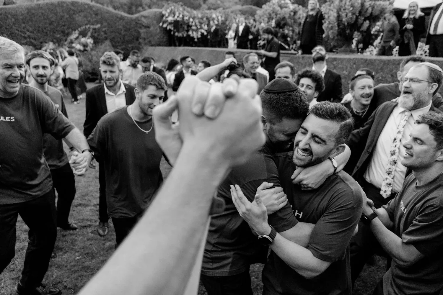 Black and white photo of a group of people celebrating outdoors, some hugging and smiling, with others in the background also smiling, during a joyful gathering or event.